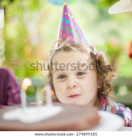 garden party with family for little girl\'s birthday, kid makes a wish and blows out the candles, the garden is decorated with balloons and colors are bright