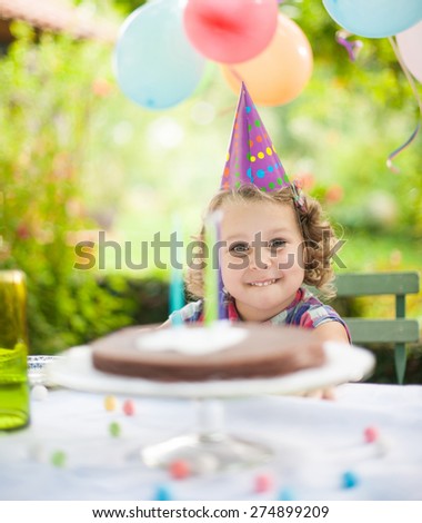 Garden party for the birthday girl. Smiling kid facing her cake at the table