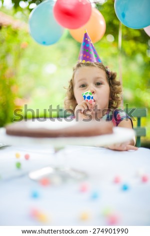 portrait of a little girl in a garden party for her birthday, she wears a funny hat and the garden  is decorated with balloons