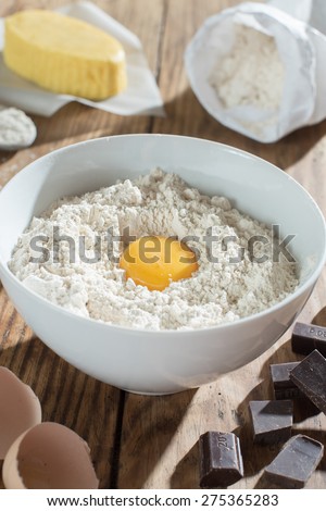 ingredients to make a cake on a wooden table, a bowl flour, butter, eggs and chocolate