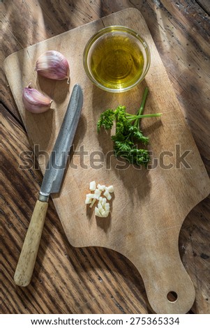 still life, a knife, garlic, oil and  parsley on a wooden board
