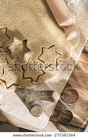 Top view, cookie cutter on cake dough and rolling pin on a wooden board