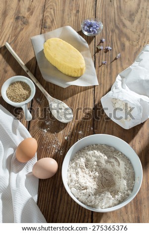 top view, ingredients to make a cake on a wooden table, a bowl flour, sugar, butter, eggs and napkin