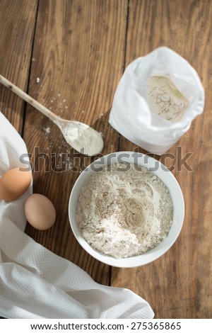 top view, ingredients to make a cake on a wooden table, a bowl flour, eggs and napkin