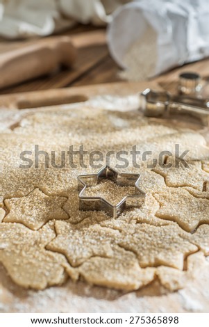 Closeup on cookie cutter on cake dough and rolling pin on a wooden board