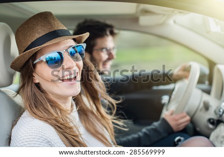 Young couple in his car, happy to drive on a country road, focus on the woman