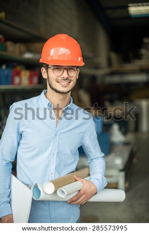 looking at camera, a young architect with a helmet on his head on an industrial site