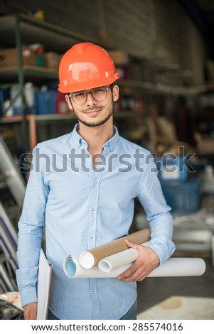looking at camera, a young architect with a helmet on his head on an industrial site