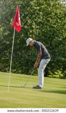 Vintage style, Portrait of a nice man surveying his putt on the fourteenth hole.  He is looking at the ball, wearing a cap and a sportswear outfit. A red flag is marking the hole