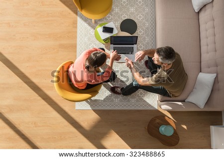 Top view of a man and woman in casual clothes. They are sitting in a stylish vintage living room with wooden floor They are discussing some new project and searching the internet on a laptop