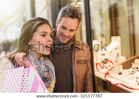 Stylish couple is looking at wedding rings. A grey hair man with beard and a woman with two shopping bags are standing in front of a jewelry shop. They are looking at the shop window.