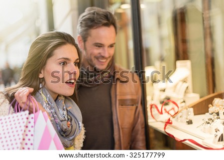 Stylish couple is looking at wedding rings. A grey hair man with beard and a woman with two shopping bags are standing in front of a jewelry shop. They are looking at the shop window.
