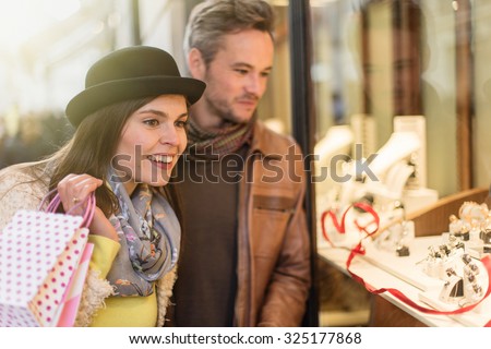 Trendy couple is looking for valentine\'gifts. A grey hair man with beard and a woman with a black hat are standing in front of a jewelry shop. They are looking at the shop window.