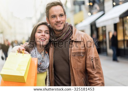 Portrait of a stylish couple doing their shopping in the city center The grey hair man with beard is wearing a leather coat and the woman a yellow top and two shopping bags, they also have scarfs
