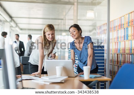 Assistant and partner coffee meeting. Focus on two women in her 30s and 40s who are standing in front of a laptop and two white coffee cup, in a luminous open space looking at balance sheets