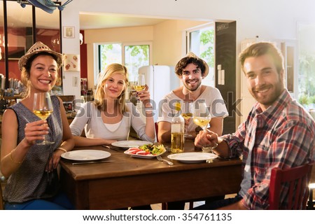 Friends in their 30s having a nice aperitif on a rustic wooden table in a lovely house. They are holding their high glasses of white wine. There are tomatoes mozzarella for starters.