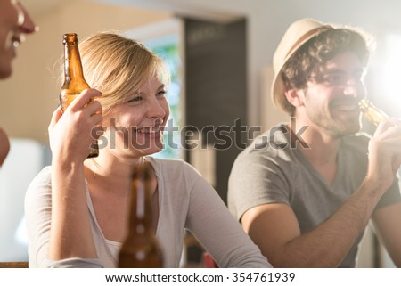 Friends having a drinks on a sunny evening. A blonde girl and a boy with beard and hat are sitting close to each other in a cozy house with beers and tortilla chips. They are wearing casual clothes