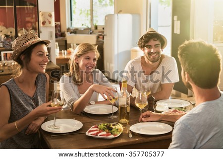Friends in their 30\'s having a nice aperitif on a rustic wooden table in a lovely house. They are having fun and talking in front of glasses of white wine and tomatoes mozzarella - real people