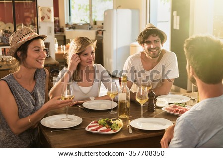 Group of friends having a nice aperitif on a rustic wooden table in a lovely house. They are having fun and talking in front of glasses of white wine and tomatoes mozzarella - real people