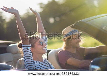 Young couple in his convertible car, happy to drive on a country road, focus on the woman. Shot with flare