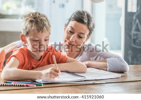 Young boy doing his school homework with his mother, at home, he is writing on a book