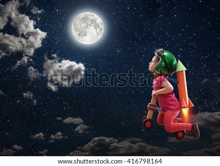A childhood dream, the cute little girl flying to the moon on her bike, she wears a helmet and has made a cardboard rocket hooked on her back