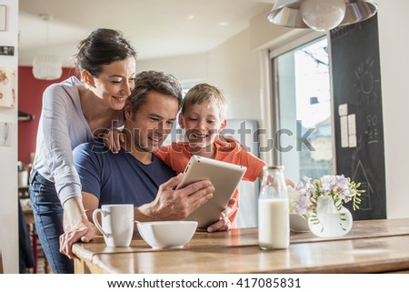 A modern family using a digital tablet while having breakfast in the kitchen, mom,  dad and their eight year old son