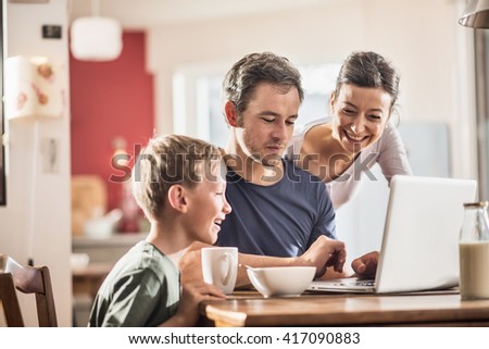 A modern family using a laptop while having breakfast in the kitchen, mom,  dad and their eight year old son