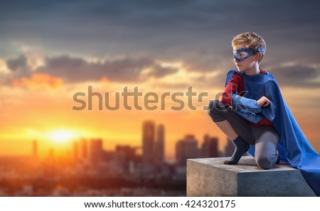 At sunset, a little boy dressed as superhero watches over the city. he strikes a pose on a pedestal above the city