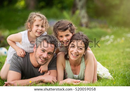 Happy family in a park, Daddy, mommy and their two cheerful daughter are lying on the grass while they are looking at camera. Shot with flare