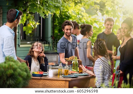 Young people having fun on the terrace, drinking beers and chatting while their friends serve the meat roasted on the bbq. Shot with flare