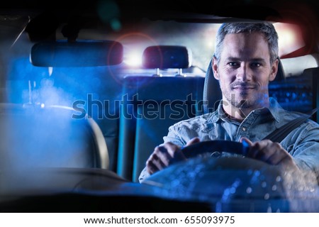 Front view. Portrait of a handsome man driving his car at night in the rain. The traffic lights behind him