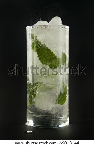 Soda water in glass with ice and mint on black background.