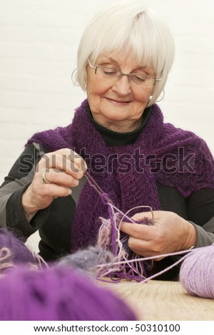 Portrait of active senior woman sorting out the tangle mess of woollen threads