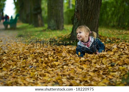Small happy girl with two funny ponytails lies at the yellow leaves