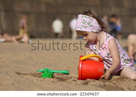 Small beauty girl play on sand with green scoop, sand pie mould and red bucket.