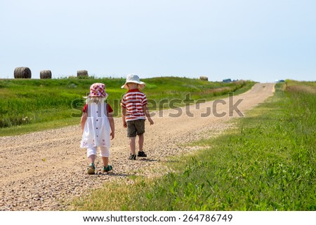 blonde haired brother & sister walking away down a country road
