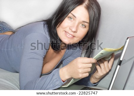 Pretty woman relaxing with laptop and newspapers on couch