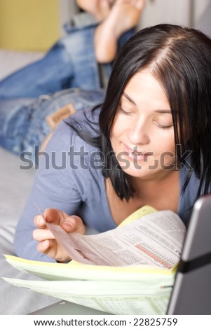 Pretty woman relaxing with laptop and reading newspapers on couch