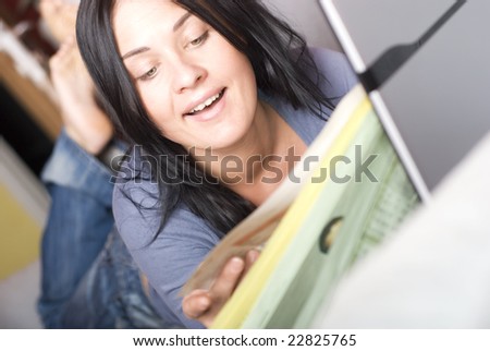 Pretty woman relaxing with laptop and readingnewspapers on couch