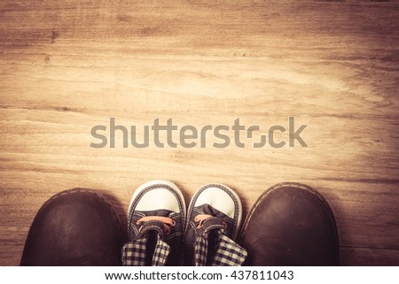 Daddy's boots and baby's sneakers, on wood background, fathers day concept.vintage color