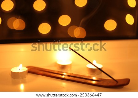 Aromatic sticks with smoke in the dark near the small burning candles on the window with bokeh