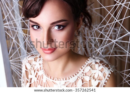 Close-up portrait of beautiful brunette in white lace dress on white interior background