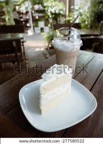 Coconut cake on white plate and cup of ice coffee on wooden table.( Vintage effect style picture)