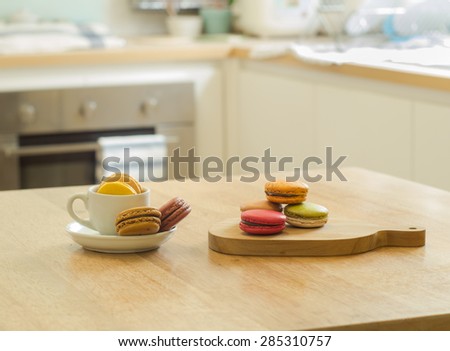 Colorful French macarons in cup and wooden tray on wooden table in a kitchen
