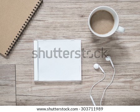 Top view of blank compact disc (CD) with cover, earphones, notebook and coffee on wooden background ( Space for picture and text )