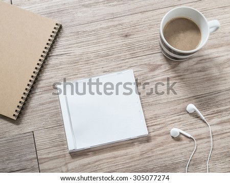 Top view of blank compact disc (CD) with cover , earphones, notebook and coffee on wooden background