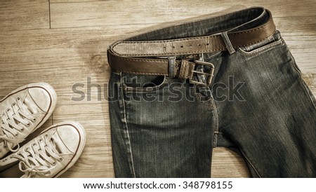 Top view of blue jeans with leather belt and dirty white sneaker shoes  on the wooden background