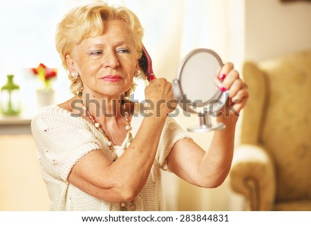 Smiling elderly woman comb hair and looked in the mirror