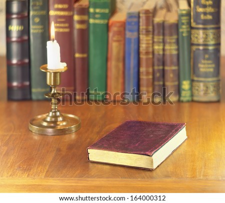 old book with golden edge and leather cover and vintage brass candlestick with alight candle